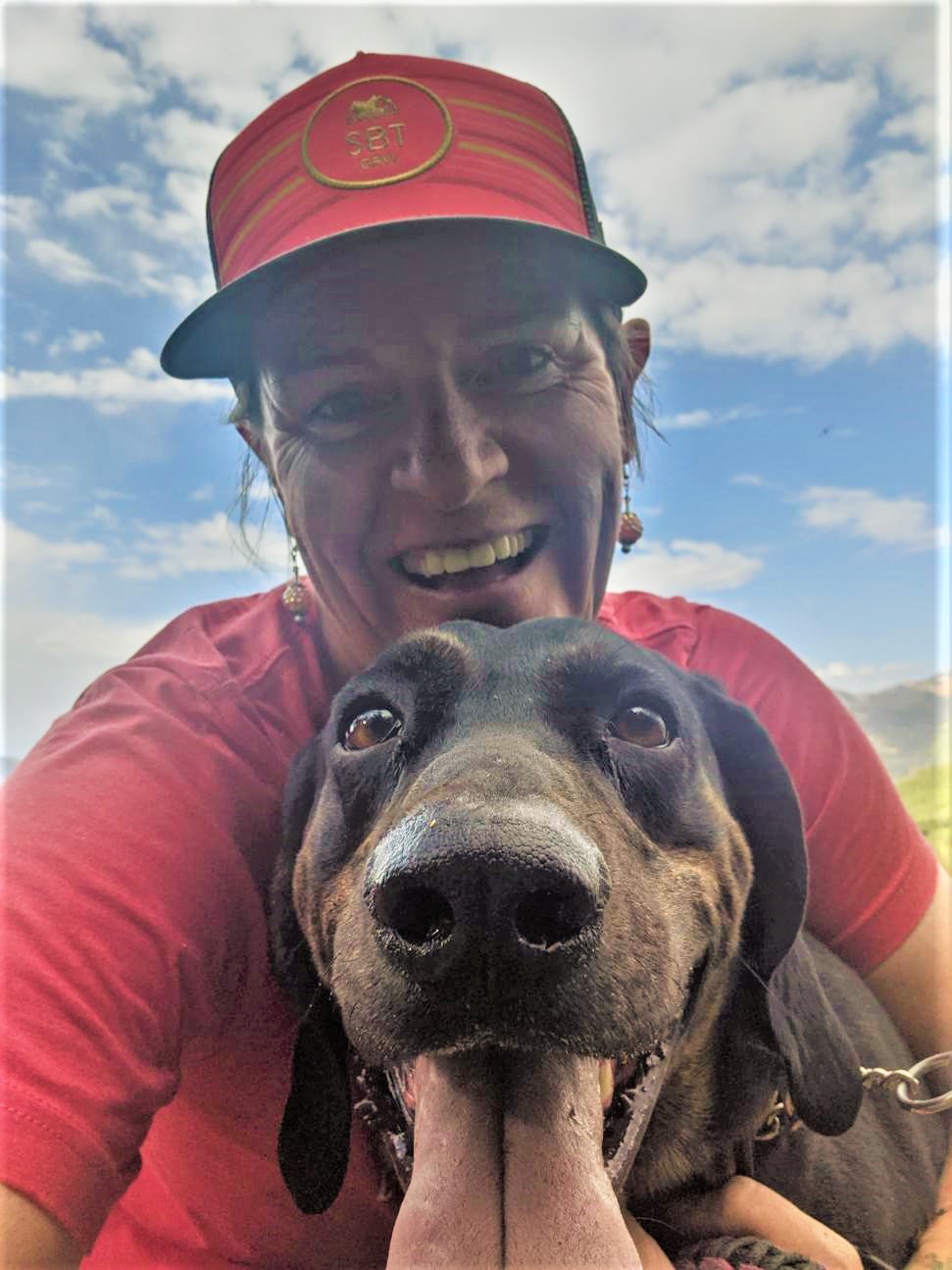 Wild Bunch Desert Guides Laurel Darren smiles widely while hugging her Plott Hound Daisy Mae during a Lake City Hiking Club hike in the breathtaking surroundings of Colorado's San Juan Mountains.