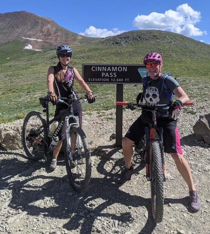 With Colorado's San Juan Mountains providing a beautiful backdrop, Laurel Darren (right) and Lake City local Lydia McNeese pose on their mountain bikes to celebrate reaching Cinnamon Pass. Darren's adventures. part of her summer vacation, also offer daily reminders about her small business, Wild Bunch Desert Guides.