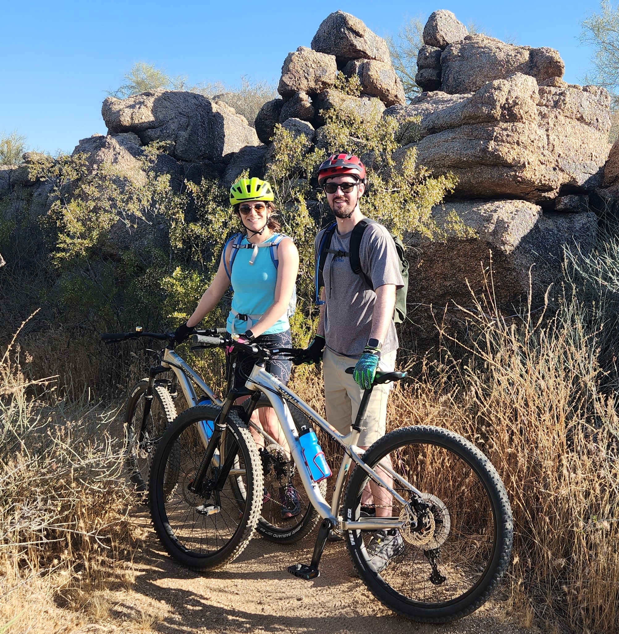 A couple on a Wild Bunch Phoenix mountain biking tour stop for an early-morning photo amid the rocky backdrop and sage brush of the Sonoran Desert.