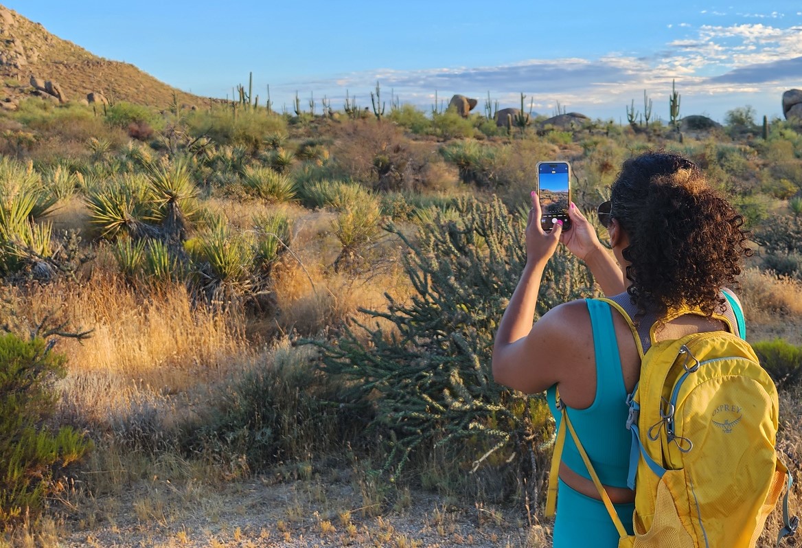 A Phoenix hiking tours guest pauses to take a memorable vacation picture of a breathtaking backdrop in the Sonoran Desert.