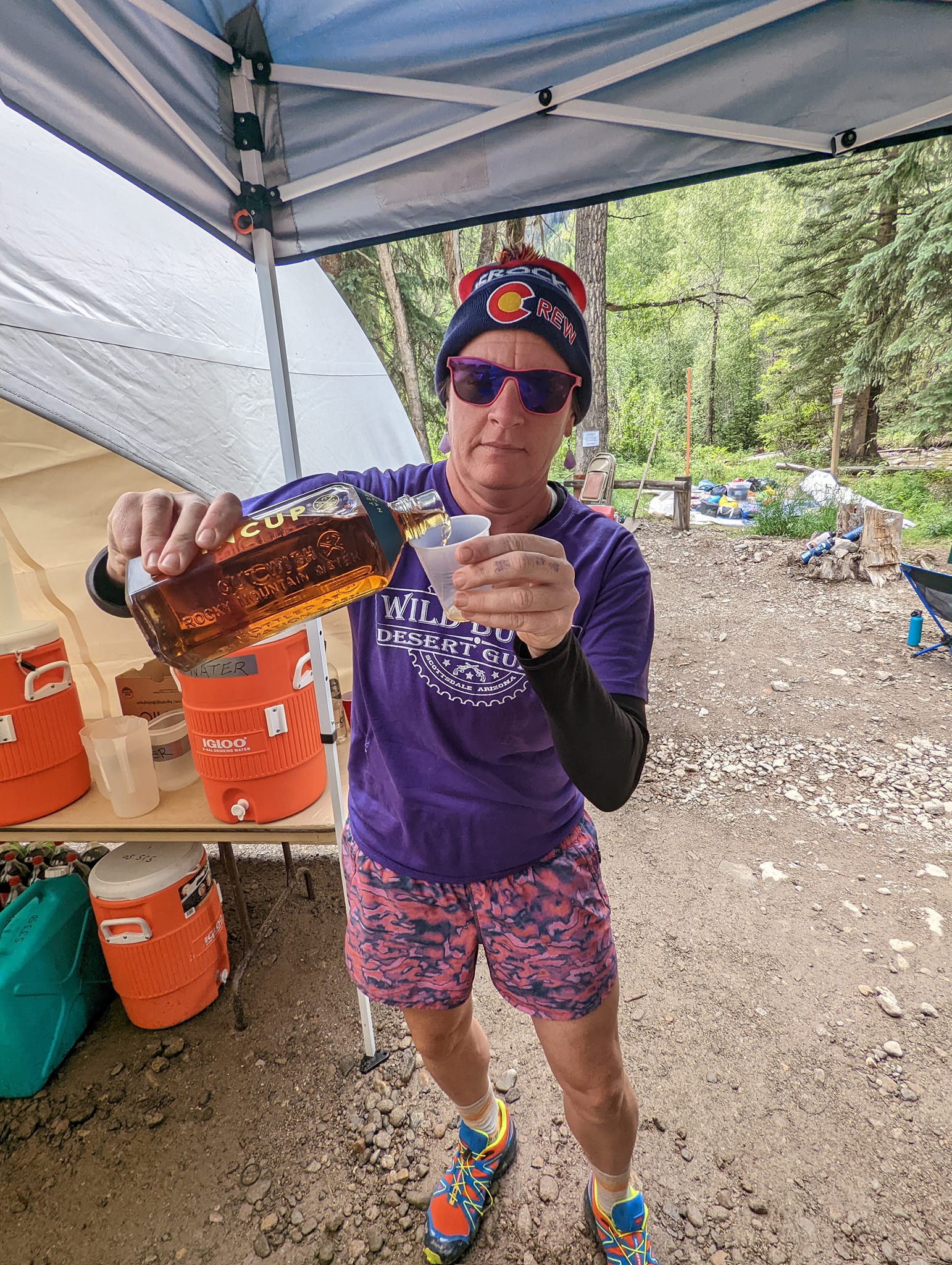 Laurel pours one of the Tin Cup Shots offered to participants at the Sherman Aid Station during the Hard Rock 100 endurance race.