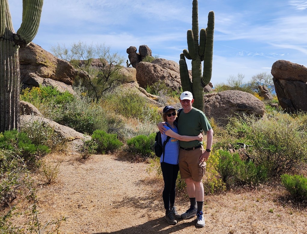 A couple hiking with the Wild Bunch pauses for a hug in the scenic Sonoran Desert for a memorable vacation photo.