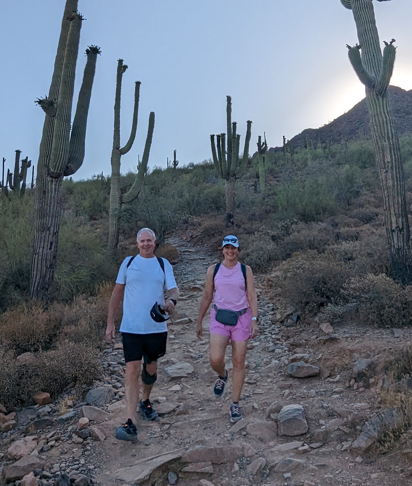 A couple hiking in the early-morning hours descend a hill full of cactus. During the summertime heat, the early bird enjoys the beauty of the Sonoran Desert to avoid the worst of the triple-digit heat.