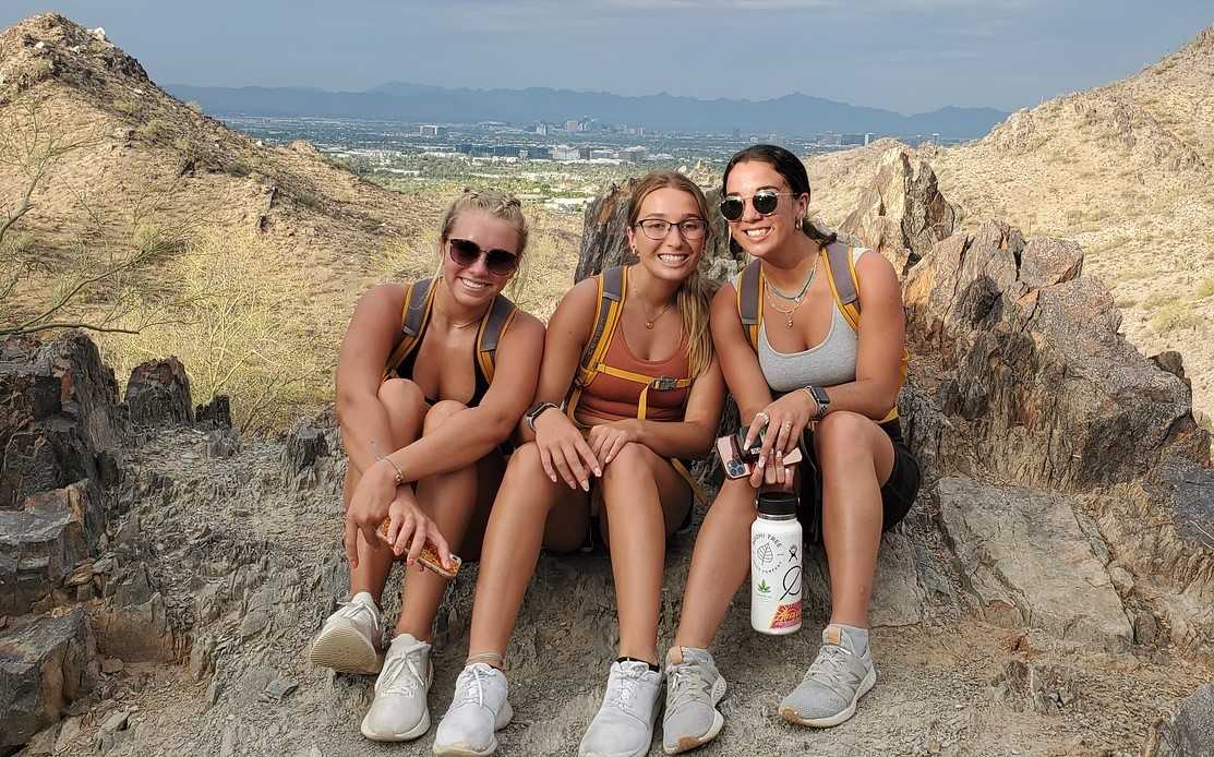 A trio of friends pause for a picture with a beautiful vista in the background during one of the Phoenix hiking tours offered by the Wild Bunch Desert Guides.