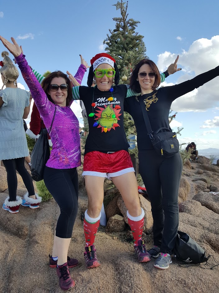 Laurel Darren (center), owner of the Wild Bunch Desert Guides, celebrates in a Yuletide costume with a pair of hiking guests in front of the Camelback Mountain Christmas tree after reaching the summit of the Phoenix landmark.