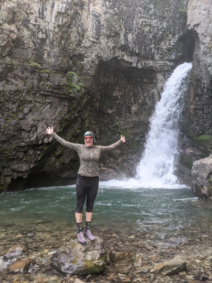 With a waterfall highlighting the cavernous surroundings, Wild Bunch Desert Guides owner Laurel Darren has her arms raised reveling in the natural beauty of her summer vacation from the daily grind of providing memorable Phoenix adventure tours.