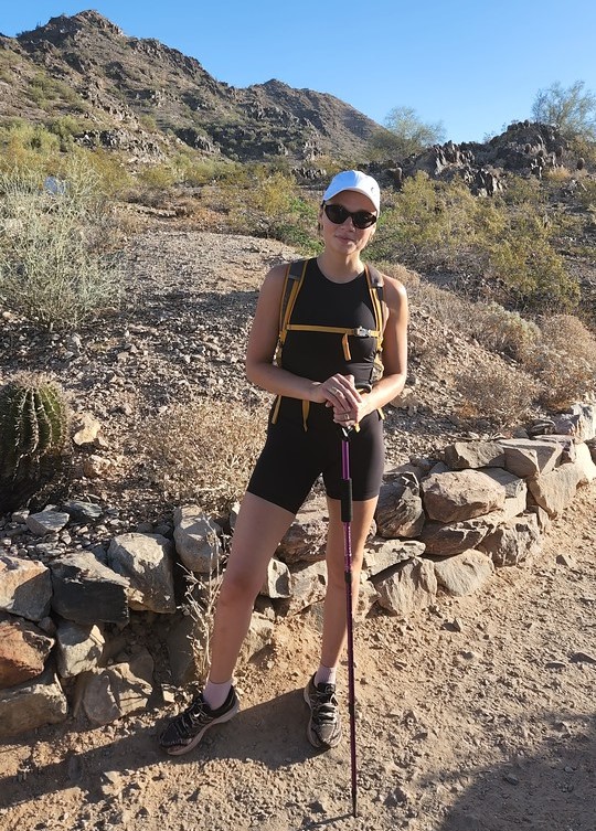 With some rocky terrain as the picturesque backdrop, a solo hiker flashes a wide smile while enjoying a guided hiking tour in Phoenix with the Wild Bunch Desert Guides., 