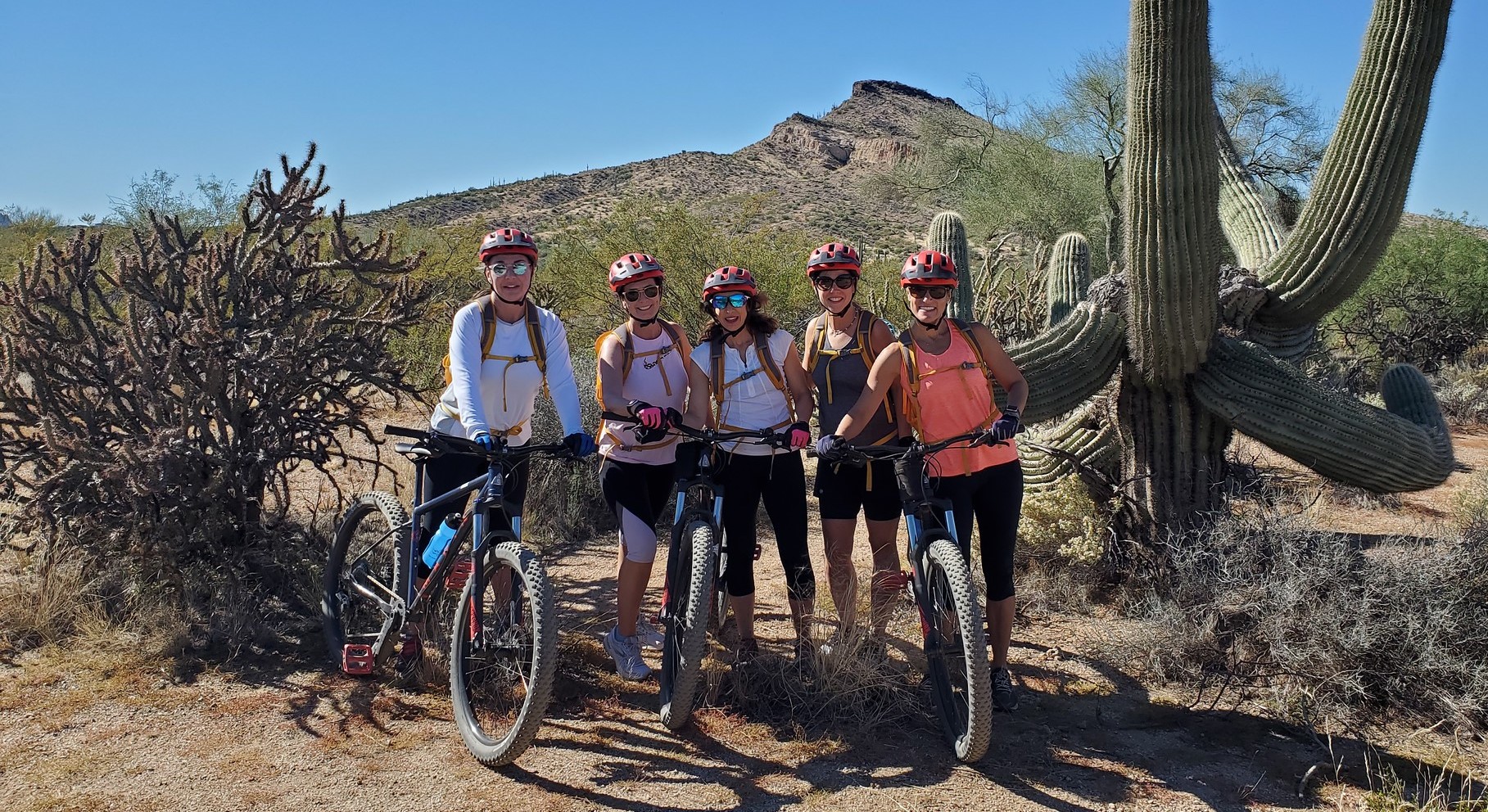 Five female friends pause during a Wild Bunch Desert Guides mountain bike ride in Scottsdale for a picturesque photo next to a cactus with a rocky cliff facing as the breathtaking backdrop. The Thanksgiving holiday only helps to remind that friends and family are among the most cherished blessings to celebrate.
