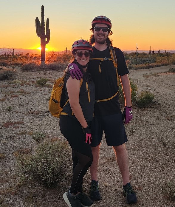 With an old west landscape as a backdrop, a couple pauses for a picture in front of a colorful Arizona sunset on one of the romantic sundown Phoenix hiking tours from the Wild Bunch.