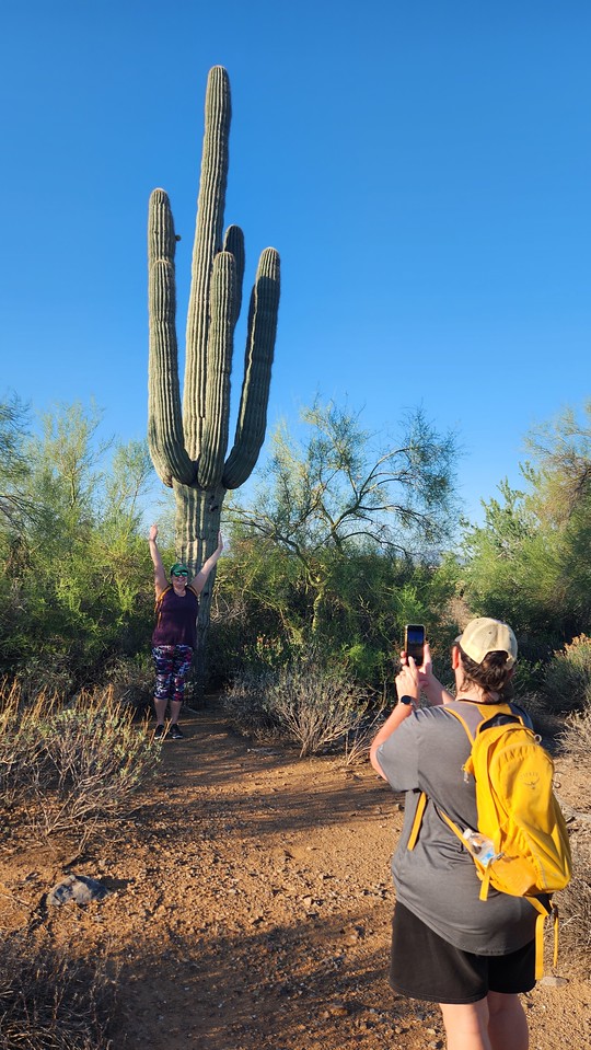 Arms raised in front of a majestic Saguaro Cactus, as captured in this photo by friends, is a regular visage during Phoenix hiking tours with the Wild Bunch Desert Guides.