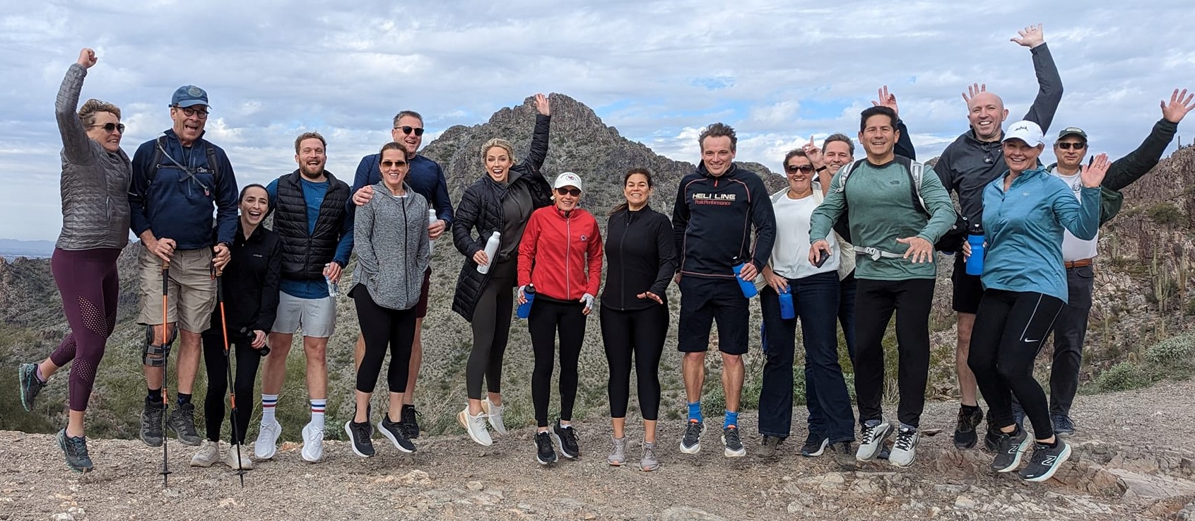 A Phoenix hiking tours group jumps for joy together in front of a scenic backdrop during a adventure with the Wild Bunch Desert Guides.