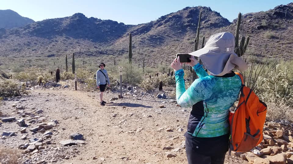 A wife takes a picture of her husband with a breathtaking backdrop behind him during one of the Phoenix hiking tours from the Wild Bunch Desert Guides.