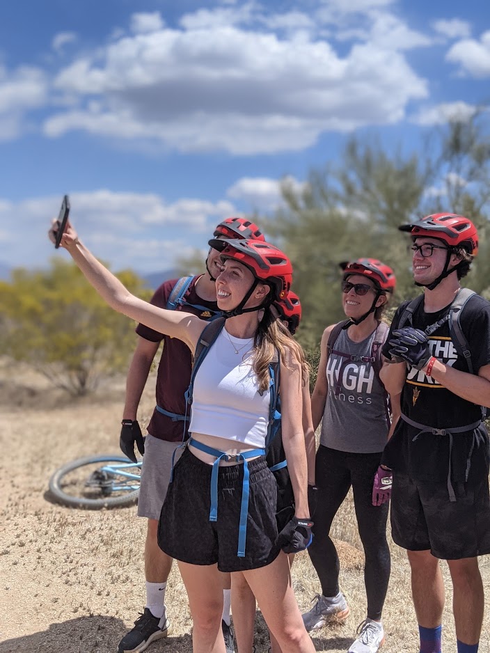 A young woman smiles into her cellphone camera while posing with three of her family members for a 